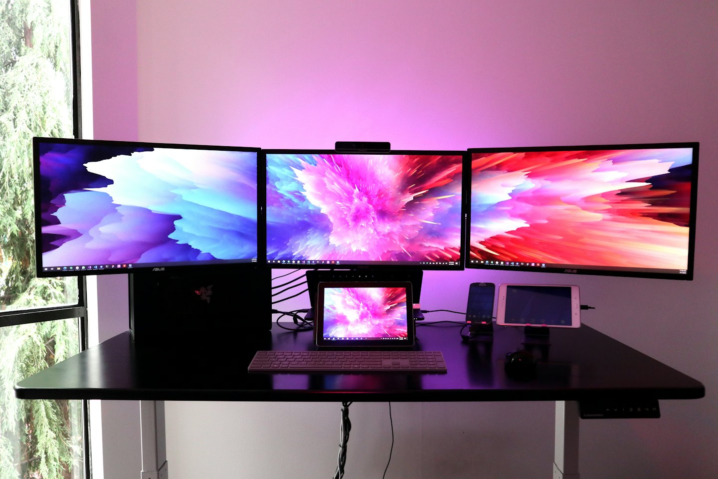 Three large monitors, tablet, and smartphone on a desk with abstract art.