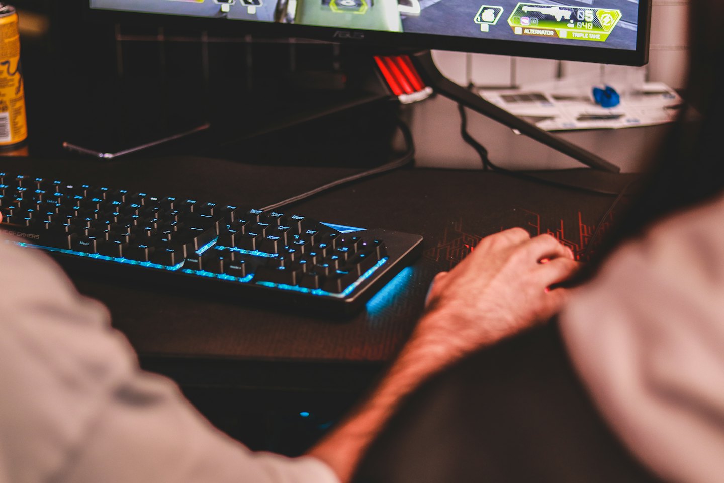 Hands using a backlit gaming keyboard and mouse on a wooden desk.