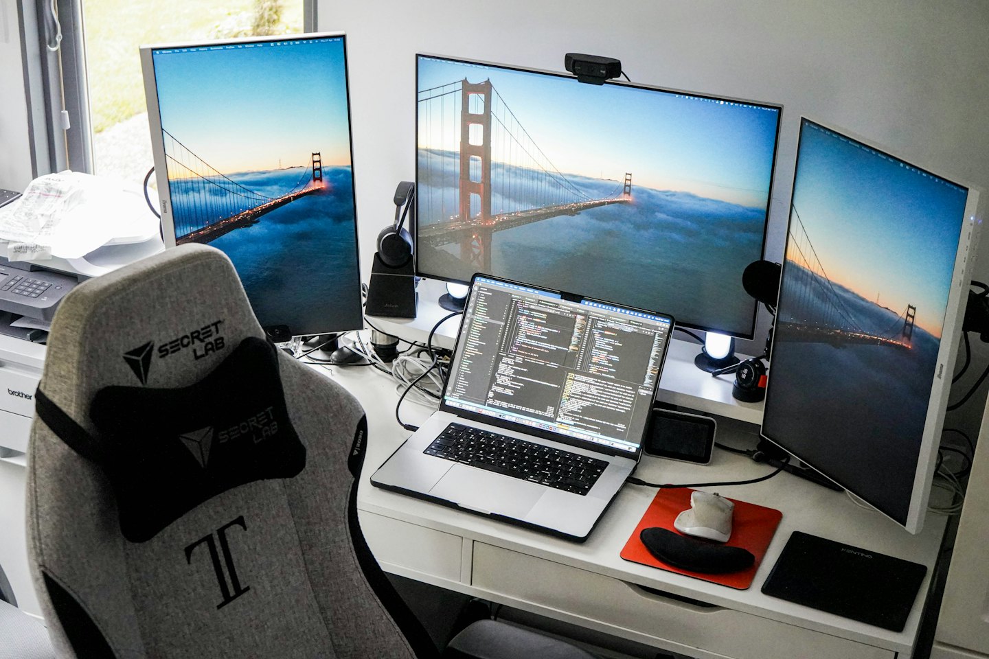 Modern multi-monitor desk setup with Golden Gate Bridge wallpaper and gaming chair.