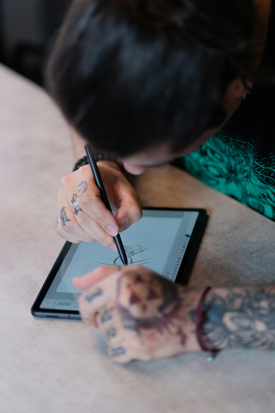 Tattooed hands sketch on a digital tablet with a stylus.