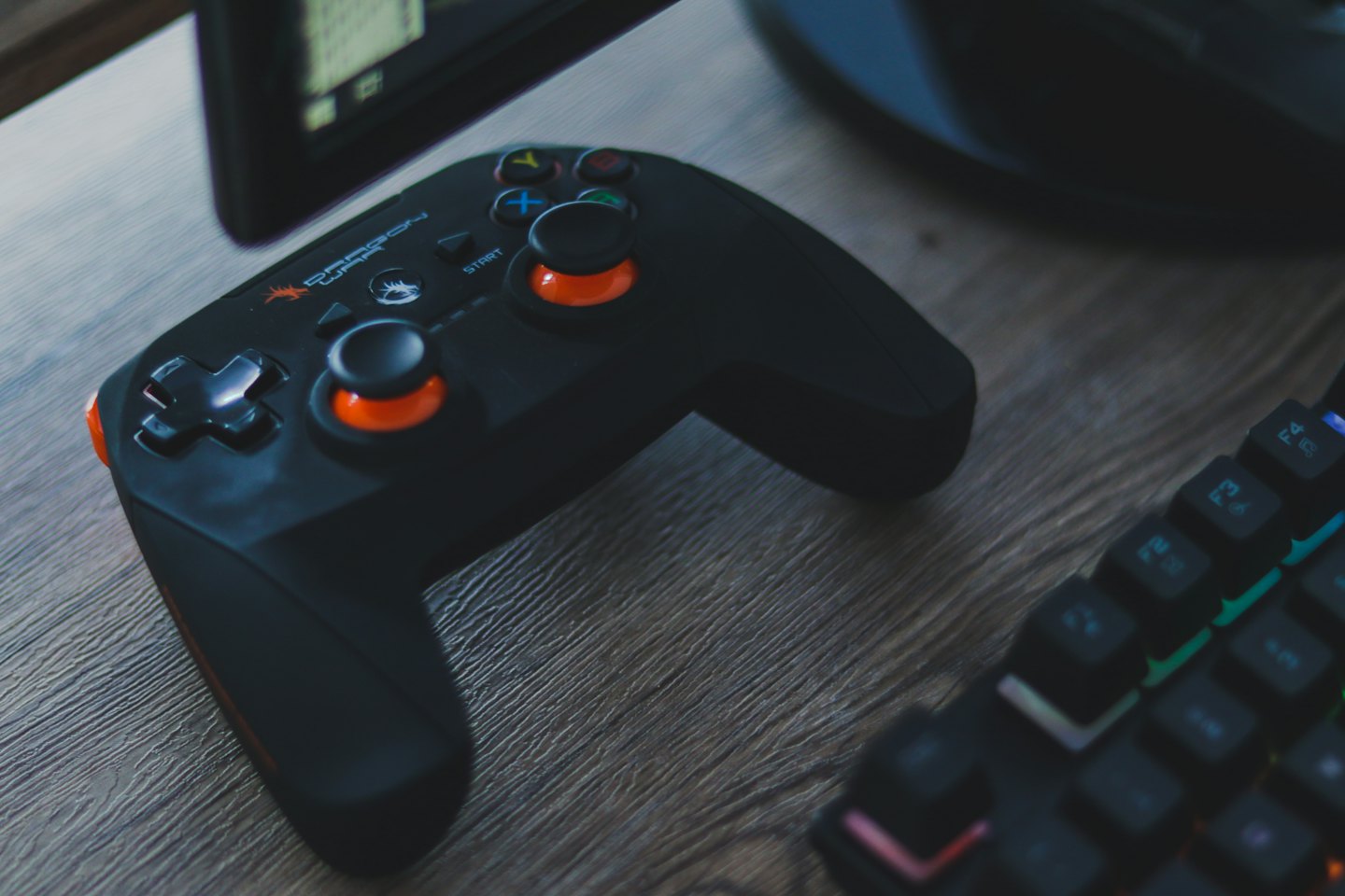 Black video game controller with orange accents on a wooden desk.